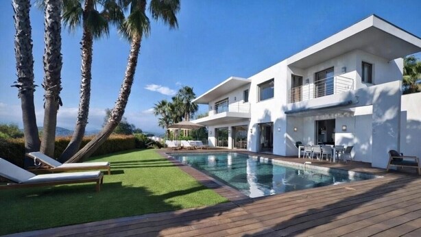 A modern two-story house with a swimming pool, palm trees, and a deck.