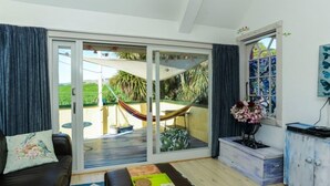 Een woonkamer met een bank, een salontafel, een hangmat en een schuifdeur die leidt naar een buitenruimte met een hangmat en groen.