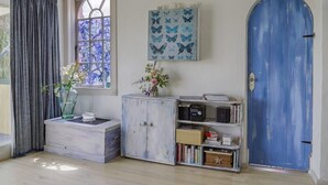 Een kamer met een blauwe deur, een raam met een glas-in-lood ontwerp, een boekenplank en een klein kastje.