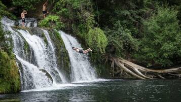 Een waterval met twee mensen bovenaan en één persoon in de lucht.