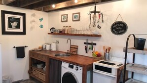 A compact kitchen with a washing machine, a microwave, and a stove. There are shelves with jars and glasses, and a welcome sign. - Kokako Lodge Wanganui (Wanganui Township)