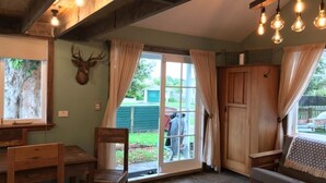 A rustic interior with a wooden dining table, chairs, a sofa, and a large window with curtains. - Kokako Lodge Wanganui (Wanganui Township)