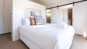 A bedroom with a bed, pillows, a framed picture, and a towel stack. - Blackpool Boathouse - Pool & Spa & Walk to Oneroa (Oneroa)