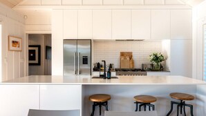 A modern kitchen with a large island, stainless steel appliances, and bar stools. - Blackpool Boathouse - Pool & Spa & Walk to Oneroa (Oneroa)