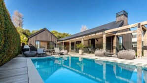 A modern house with a swimming pool, outdoor seating, and a wooden deck. - Blackpool Boathouse - Pool & Spa & Walk to Oneroa (Oneroa)