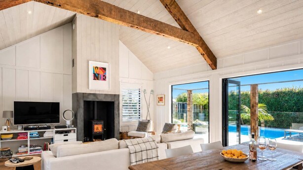 A modern living room with a fireplace, a television, and a dining area with a table and chairs. - Blackpool Boathouse - Pool & Spa & Walk to Oneroa (Oneroa)