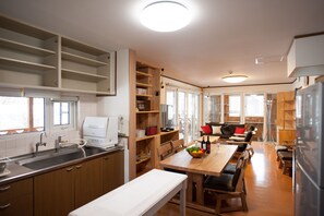 A modern kitchen with wooden cabinets, a built-in oven, and a dining area with a long table and benches.