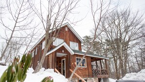 A wooden cabin with a porch and a stone foundation, surrounded by snow and trees. - Hakuba Syunrokuan (Hakuba)