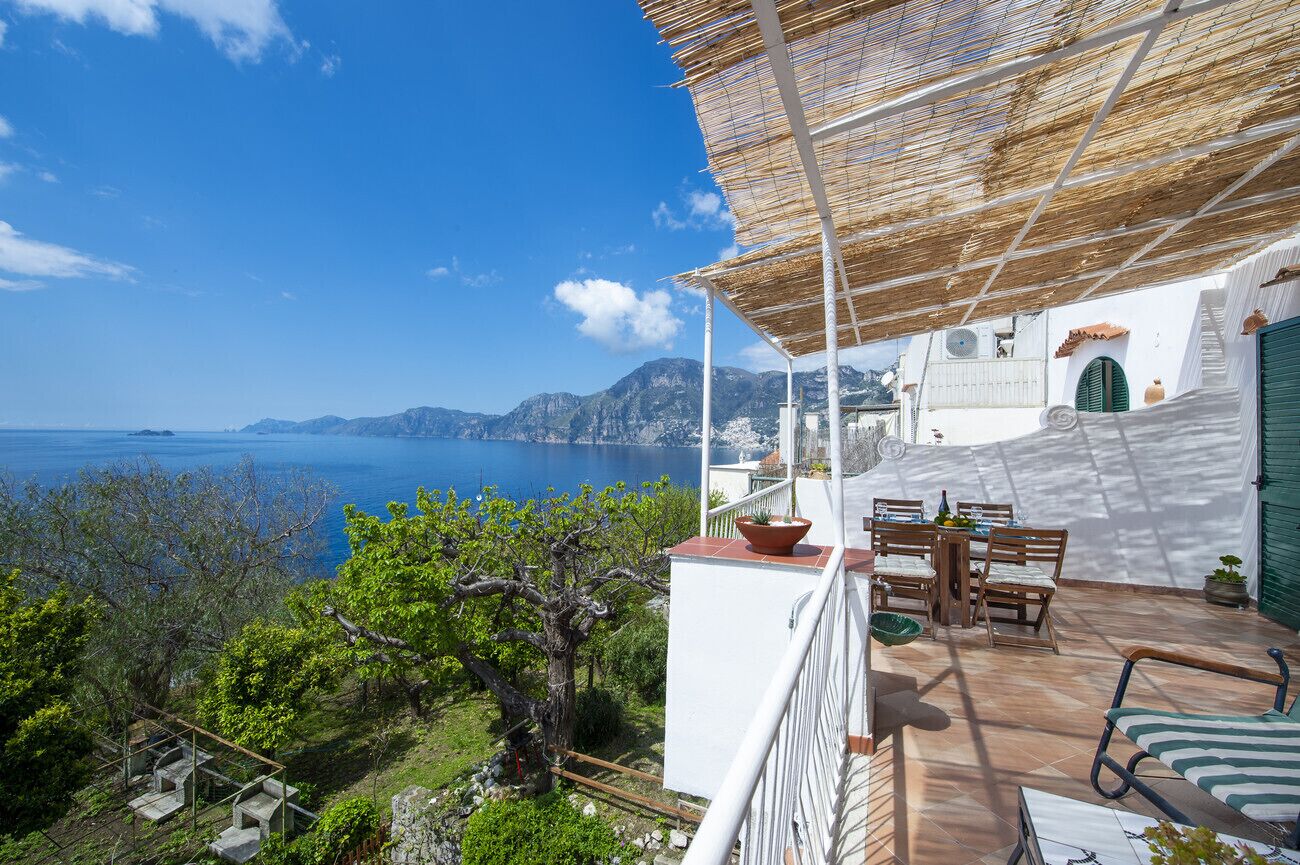 Une terrasse avec une table et des chaises, offrant une vue sur un paysage côtier avec des montagnes et la mer.