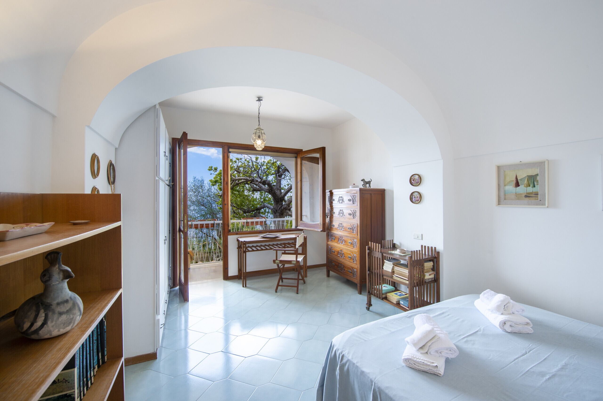 A room with a bed, a desk, a chair, a dresser, and a view of the outdoors.