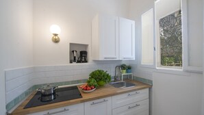 Een kleine keuken met witte kastjes, een houten aanrecht, een spoelbak, een fornuis en een raam met uitzicht op groen.