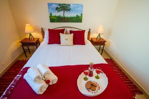 A neatly made bed with red and white bedding, two bedside tables with lamps, a tray with cookies and glasses of red drink, and a painting of a tree on the wall. - Erigone Cottage - Beautiful Ambiance (Vasa)
