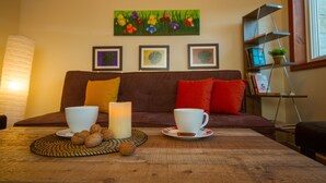 A cozy living room with a brown sofa, a table with two white cups and a candle, and a painting of flowers on the wall. - Erigone Cottage - Beautiful Ambiance (Vasa)