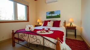 A neatly made bed with a red and white bedspread, two bedside tables with lamps, a painting of a tree, and a window with a view of trees. - Erigone Cottage - Beautiful Ambiance (Vasa)