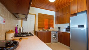 A modern kitchen with wooden cabinets, a stainless steel refrigerator, a washing machine, and a microwave. - Erigone Cottage - Beautiful Ambiance (Vasa)