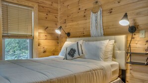 A wooden-paneled bedroom with a bed, two bedside lamps, and a macrame wall hanging.