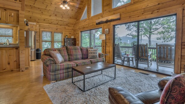 A cozy cabin interior with a plaid sofa, a coffee table, and a large sliding glass door leading to a deck.
