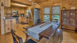 A wooden cabin kitchen with a dining table, wooden cabinets, a refrigerator, and a microwave.