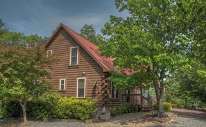 A log cabin with a red roof, surrounded by trees and a gravel driveway.