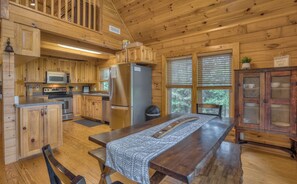 A wooden cabin kitchen with a dining table, wooden cabinets, a refrigerator, and a microwave.