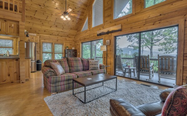 A cozy cabin interior with a plaid sofa, a coffee table, and a large sliding glass door leading to a deck.