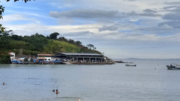A beach with yellow umbrellas, a building with a covered area, and boats in the water.