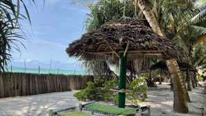 Een strand met een rieten hut, houten ligbedden en een zandstrand met palmbomen.