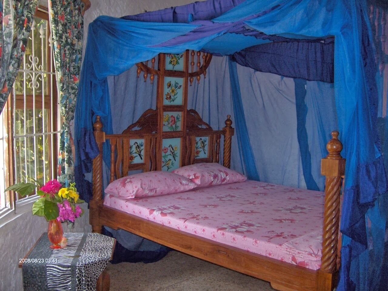 A single bed with a wooden frame and a floral bedspread, covered by a blue canopy.