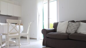 A modern living room with a grey sofa, white chairs, and a kitchen area with white cabinets.