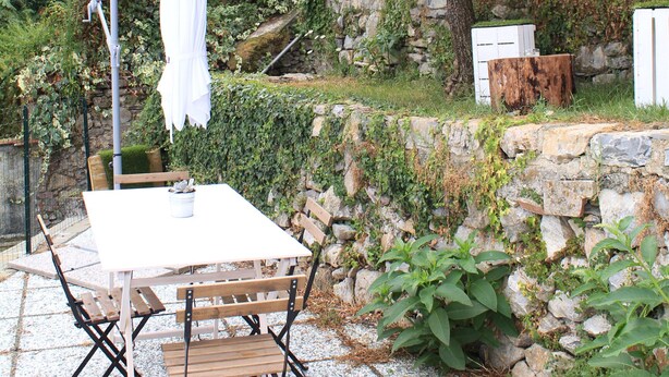 An outdoor patio with a table and chairs, a white umbrella, and a stone wall.