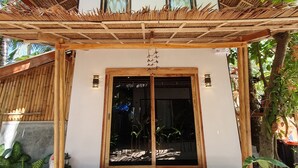A traditional wooden house with a thatched roof, a wooden porch, and a large sliding glass door. - Higala Hostel Siargao (General Luna)