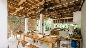 A spacious dining area with a long wooden table set for multiple people, a ceiling fan, and a brick wall in the background. - Higala Hostel Siargao (General Luna)