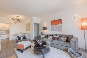 A modern living room with a grey sofa, a glass coffee table, and a dining area with a white table and chairs.