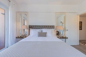 A large bed with a tufted headboard, two bedside tables with lamps, and a mirror on each side.
