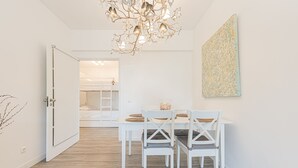 Ein moderner Essbereich mit einem weißen Tisch und Stühlen, einer Chandelüster und einem großen, abstrakten Gemälde an der Wand.