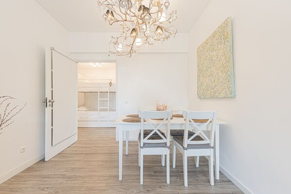 A modern dining area with a white table and chairs, a chandelier, and a large abstract painting on the wall.
