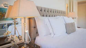 Ein ordentlich bezogenes Bett mit einer gepolsterten Kopfteile, einer Nachttischlampe und einem Spiegel, der den Raum widerspiegelt.