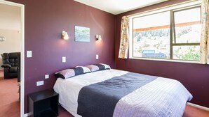 Una camera da letto con un letto, un comodino, una lampada a parete, una finestra con tende e una porta che dà su un'altra stanza.