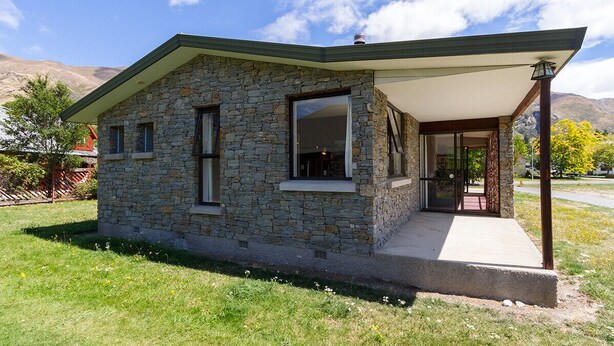 Una casa in pietra con portico coperto, una finestra interna visibile e cielo sereno.