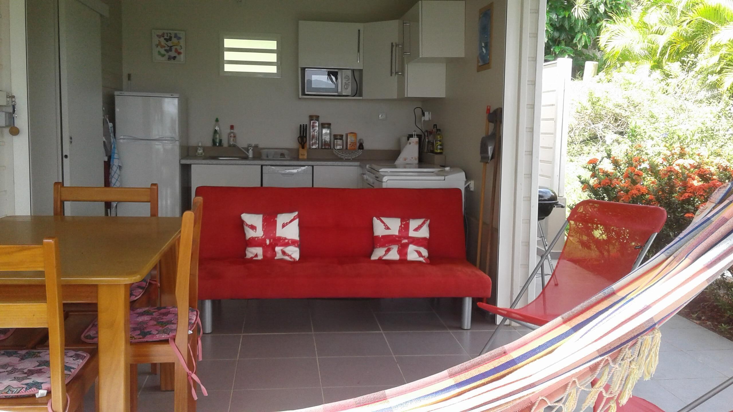 A compact living space with a red sofa, wooden dining table, and chairs, a small kitchen area, and a hammock.