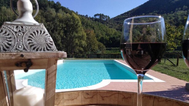 Vista de la piscina con una copa de vino tinto, un farol decorativo y montañas al fondo.