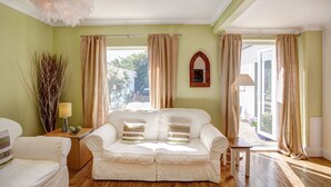 A room with a white sofa, a wooden side table, a lamp, and a view through large windows.