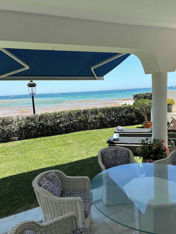 A patio with wicker furniture, a glass table, and a view of the beach.