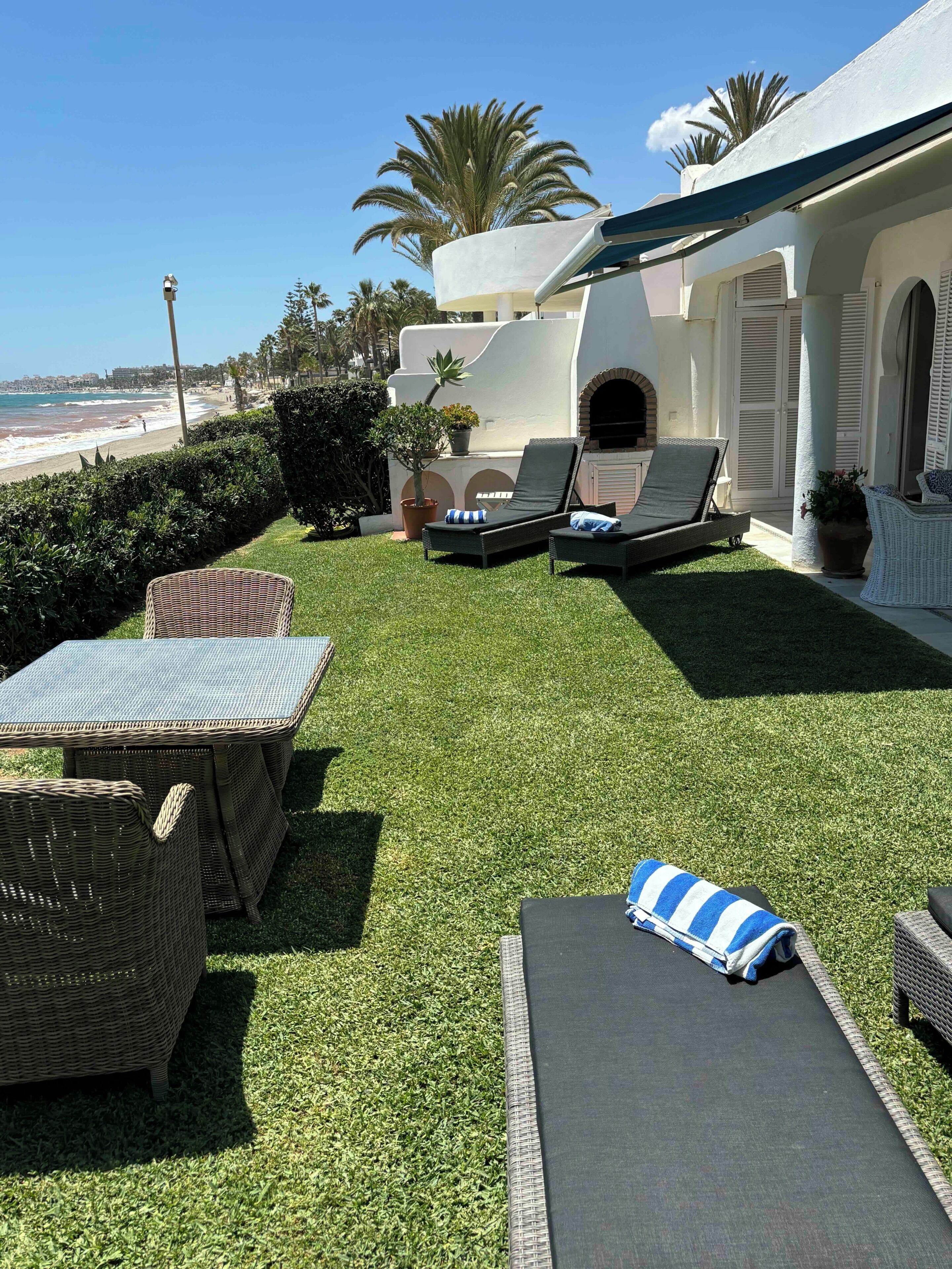 A patio with lounge chairs, a table, and a view of the beach.