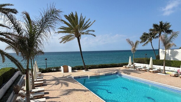 A pool with clear blue water, surrounded by lounge chairs and palm trees, with a view of the ocean. - BEACHFRONT , Central,  quiet,  parking,  pool (Marbella)