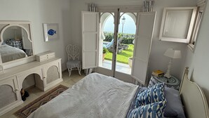 A bedroom with a large bed, a chair, a dresser, and a view of the outdoors through a glass door. - BEACHFRONT , Central,  quiet,  parking,  pool (Marbella)