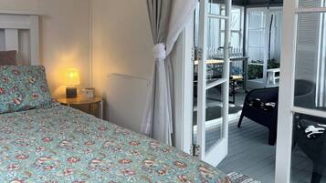 A bedroom with a bed, a nightstand, a lamp, and a view of an outdoor deck.