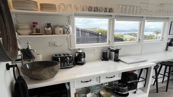 A kitchen with white cabinetry, a black kettle, and a window overlooking a landscape.