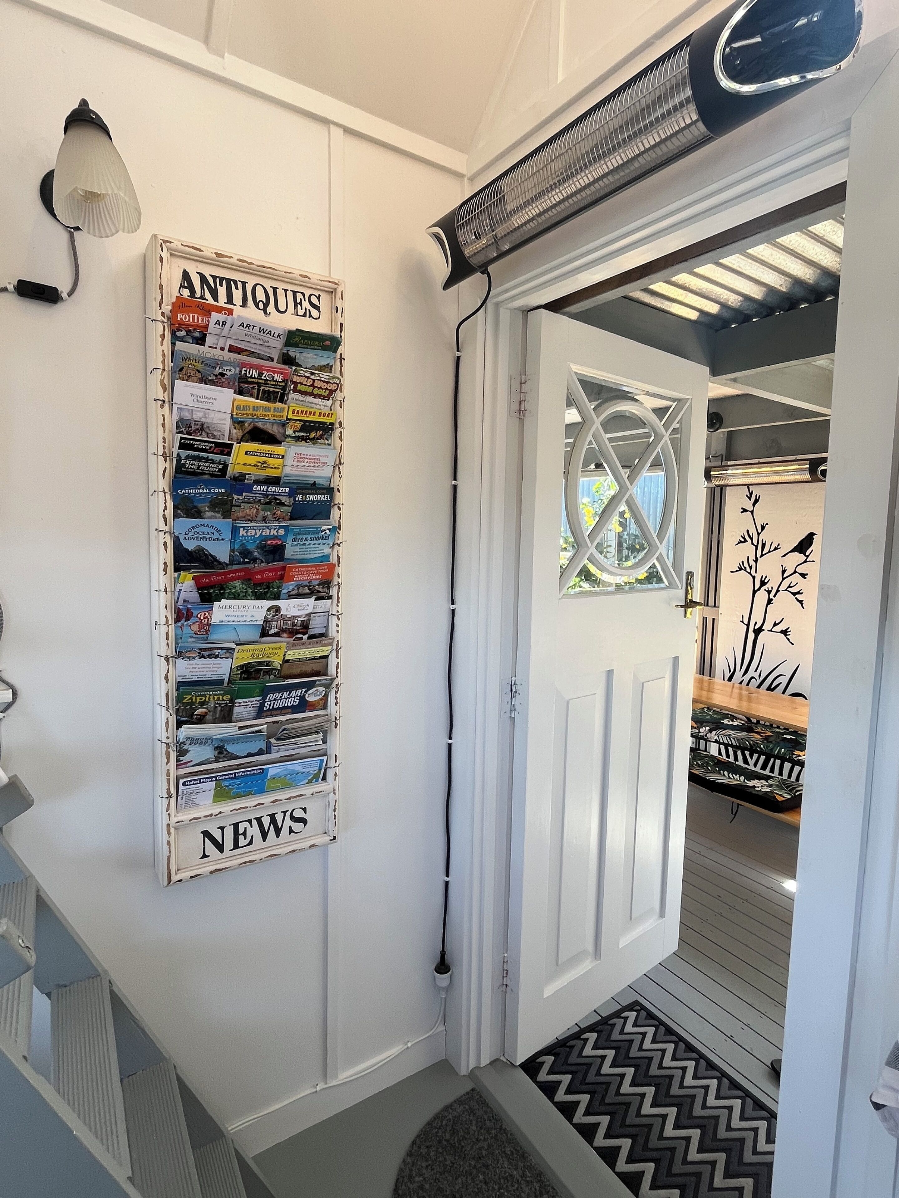 A hallway with a bulletin board labeled 'ANTIQUE NEWS' and a door leading to a room with a patterned rug.