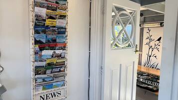 A hallway with a bulletin board labeled 'ANTIQUE NEWS' and a door leading to a room with a patterned rug.